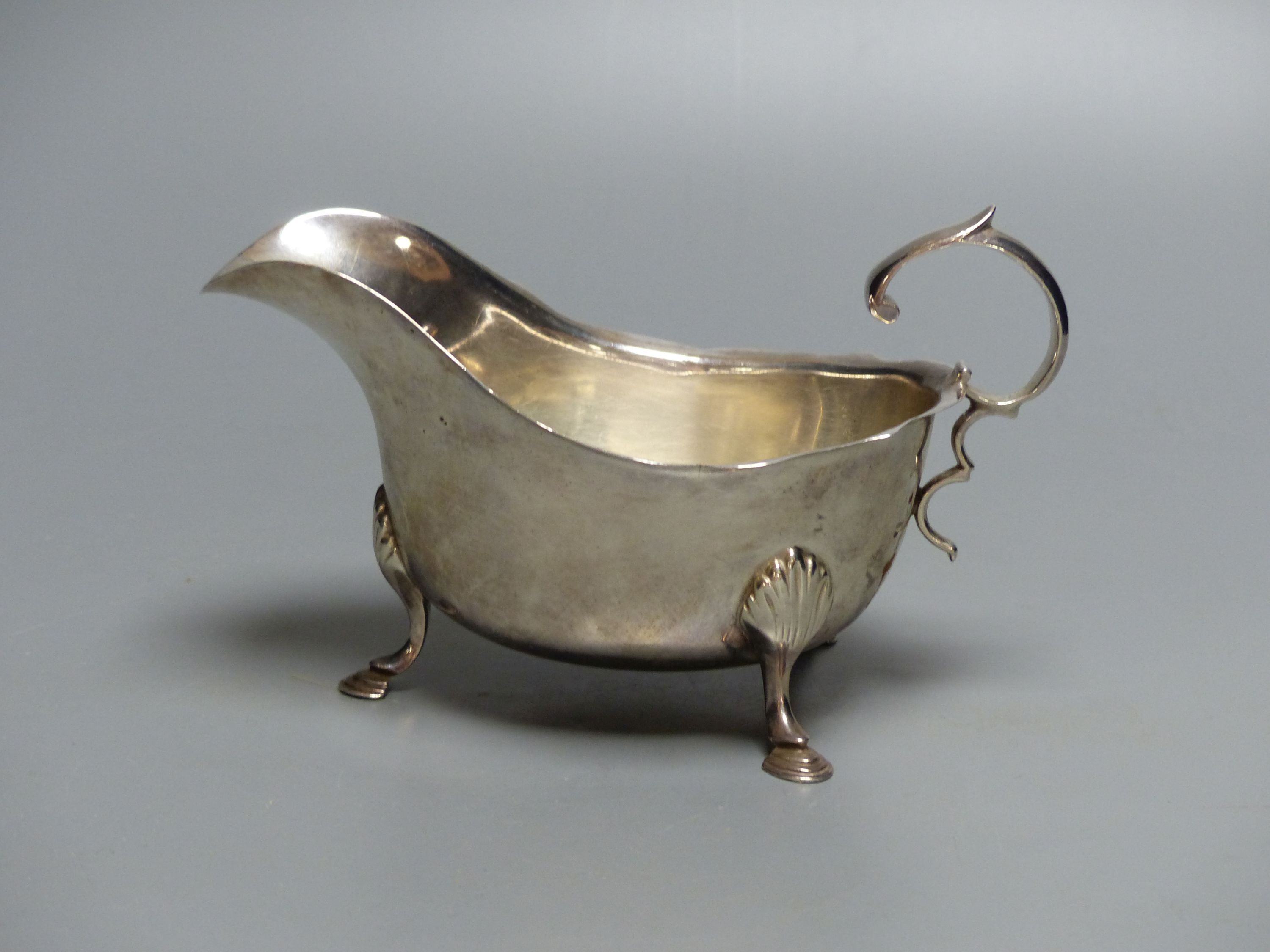 A silver sauce boat, having shaped edge, flying scroll handle and three hoof feet, marks rubbed, 4oz.